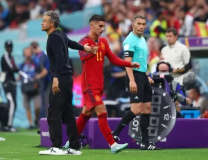 Soccer coach shakes hands with a Spain player in red as a referee watches during a match.