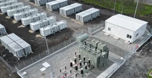 A fenced industrial yard with rows of gray shipping containers and a small white building nearby. (Aerial view)